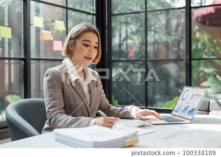 Business woman calculating monthly expenses, managing budget. Woman sitting at table using calculator to calculate tax refund, working at office with laptop on table Business woman calculating monthly expenses, managing budget. Woman sitting at table using calculator to calculate tax refund, working at office with laptop on table 100338189