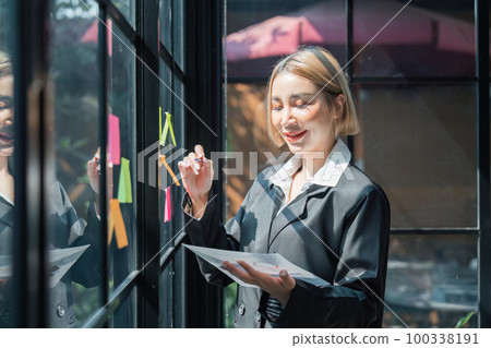 girl asian woman entrepreneur of small company putting a adhesive sticky notes in glass wall in office during analyzing formulating business strategies girl asian woman entrepreneur of small company putting a adhesive sticky notes in glass wall in office during analyzing formulating business strategies 100338191