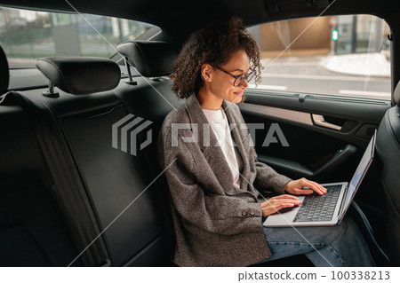 Executive woman manager working on laptop sitting car leather backseat on the way to office 100338213