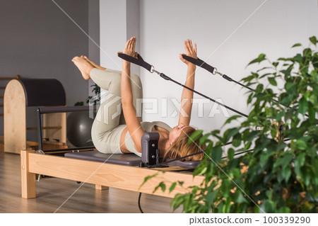 Woman training pilates on the reformer bed. Reformer pilates studio machine for fitness workouts in gym. Fit, healthy and strong authentical body. Fitness concept Woman training pilates on the reformer bed. Reformer pilates studio machine for fitness workouts in gym. Fit, healthy and strong authentical body. Fitness concept 100339290