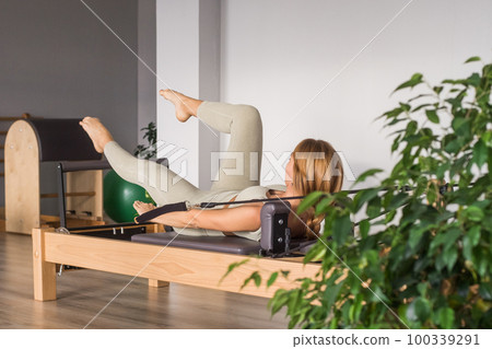 Woman training pilates on the reformer bed. Reformer pilates studio machine for fitness workouts in gym. Fit, healthy and strong authentical body. Fitness concept Woman training pilates on the reformer bed. Reformer pilates studio machine for fitness workouts in gym. Fit, healthy and strong authentical body. Fitness concept 100339291