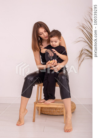 A slender mother with a little boy, is sitting next to a light wall, indoors A slender mother with a little boy, is sitting next to a light wall, indoors 100339295