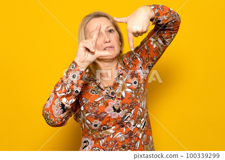 Caucasian blonde woman wearing a patterned dress making the framing gesture with a suffering face isolated on yellow studio background. Caucasian blonde woman wearing a patterned dress making the framing gesture with a suffering face isolated on yellow studio background. 100339299