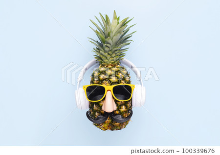 Ripe pineapple with sunglasses and headphones on blue background Ripe pineapple with sunglasses and headphones on blue background 100339676
