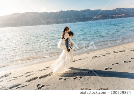 Bride and groom on their backs on the sandy beach 100339854