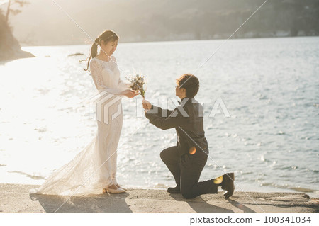 A man proposing to a woman on the beach with a bouquet 100341034