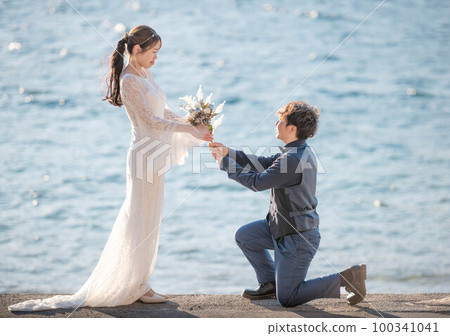 A man proposing to a woman on the beach with a bouquet 100341041