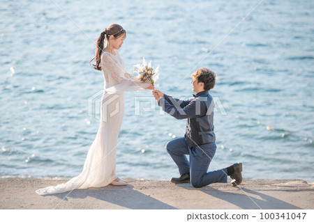 A man proposing to a woman on the beach with a bouquet A man proposing to a woman on the beach with a bouquet 100341047