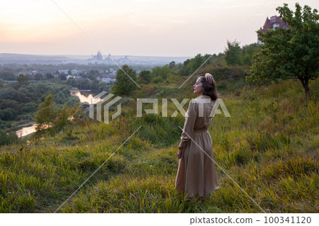 Happy woman walks at sunset on a hill overlooking the river 100341120