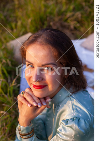 A woman in blue dress sits on a picnic in a park with panoramic view A woman in blue dress sits on a picnic in a park with panoramic view 100341321