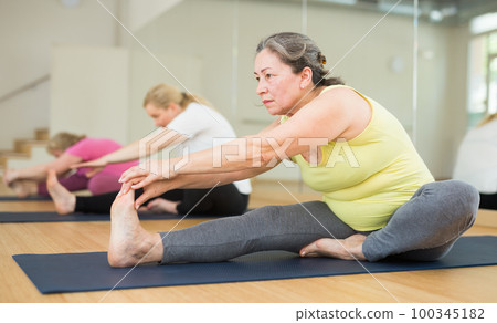 Women practicing yoga, sitting in Seated forward bend exercise, paschimottanasana pose 100345182