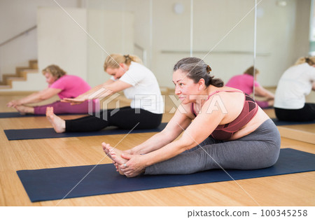 Women practicing yoga, sitting in Seated forward bend exercise, paschimottanasana pose Women practicing yoga, sitting in Seated forward bend exercise, paschimottanasana pose 100345258