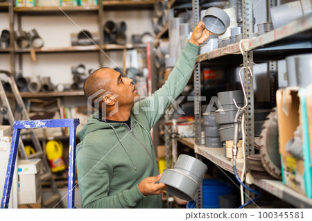 Attentive man buys plumbing plastic fittings in hardware store Attentive man buys plumbing plastic fittings in hardware store 100345581