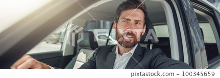 Handsome businessman in grey suit is riding behind steering wheel of car 100345659