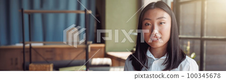 Young asian businesswoman standing at office and holding phone Young asian businesswoman standing at office and holding phone 100345678