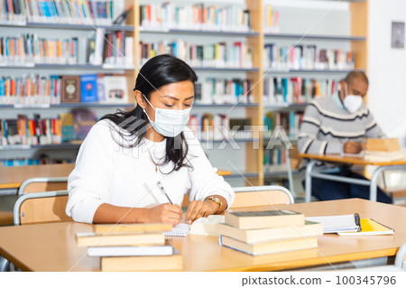 Woman wearing mask studying in public library Woman wearing mask studying in public library 100345796