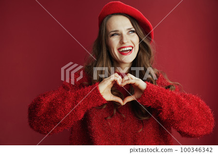 happy trendy woman in red sweater and beret showing heart hands 100346342
