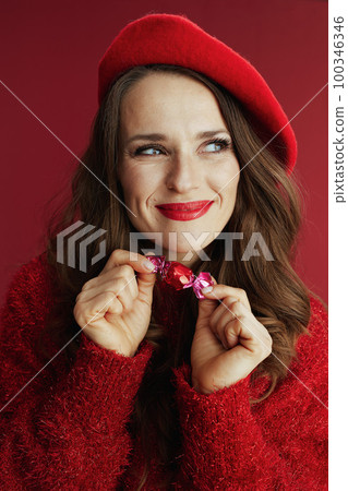 smiling stylish woman in red sweater and beret with candy 100346346