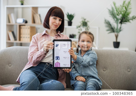 Happy lady and child buying clothes online via tablet 100348365