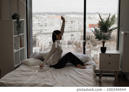 Pleasant woman stretching arms on white comfy bed Pleasant woman stretching arms on white comfy bed 100349444