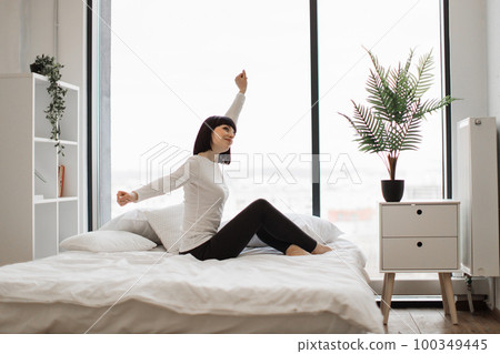 Pleasant woman stretching arms on white comfy bed 100349445
