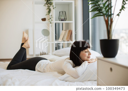Woman relaxing on bed and looking out panoramic windows Woman relaxing on bed and looking out panoramic windows 100349473