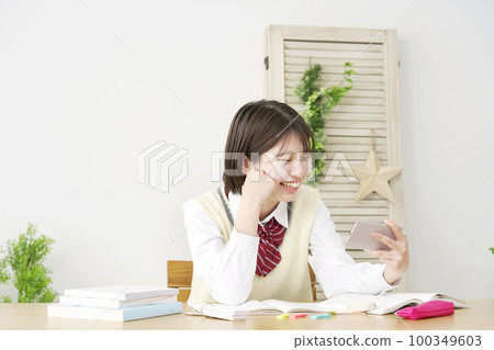 一個高中女生在家學習休息期間在她的智能手機上觀看視頻 100349603