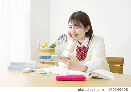 一個高中女生在家學習休息期間在她的智能手機上觀看視頻 100349608