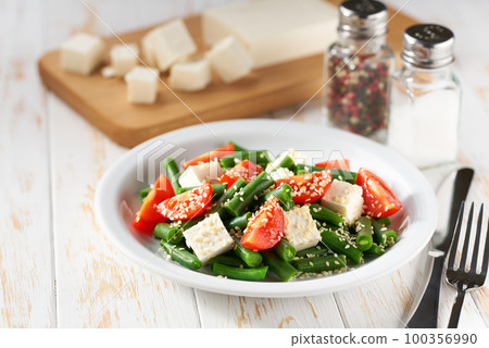 Fresh vegetarian vegetable salad with with tomatoes, feta and sesame seeds on a white wooden table, healthy food. 100356990
