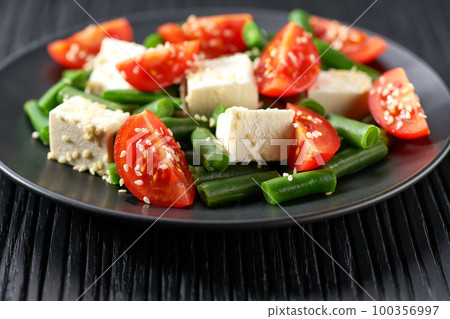 Green beans salad with feta on a black plate. Plate with delicious green beans salad on wooden table, closeup. Green beans salad with feta on a black plate. Plate with delicious green beans salad on wooden table, closeup. 100356997