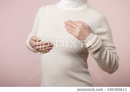 Woman hands checking lumps on her breast for signs of breast cancer on pink background. Healthcare concept. Woman hands checking lumps on her breast for signs of breast cancer on pink background. Healthcare concept. 100360611