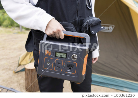 Young woman hand with portable power supply at campsite 100361220