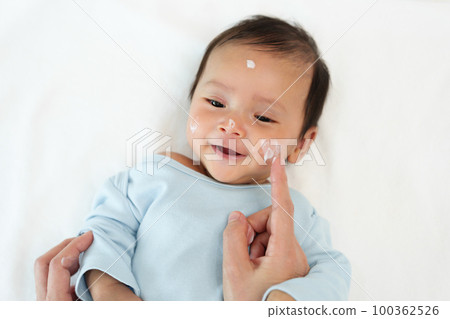 mother applying moisturizing cream on face of newborn baby mother applying moisturizing cream on face of newborn baby 100362526