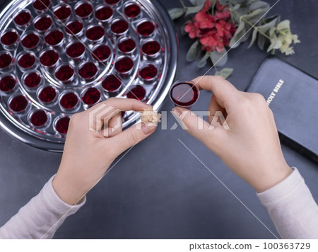 Closeup of young woman taking communion from small cups on black background 100363729