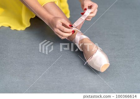 lacing of ballet shoes on the feet of a ballerina 100366614