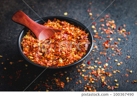 Dry chili pepper flakes. Crushed red peppers in bowl on black table. 100367490
