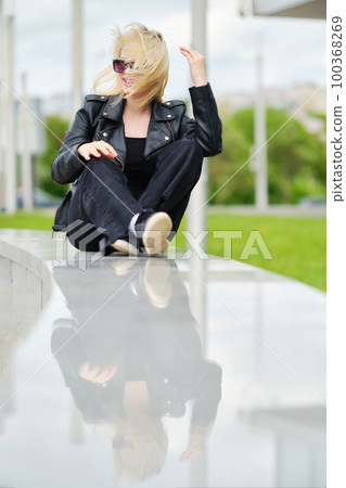 Girl in total black outfit sits on railing in windy day 100368269