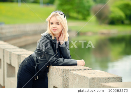 Portrait of cute teenager girl in black jeans, tank top and leather jacket outdoors 100368273