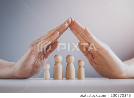 Women's hands over wooden family models on the grey background. 100370346
