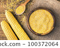 Corn grits in a wooden bowl on the background of fresh corn on the cob on a burlap. 100372064