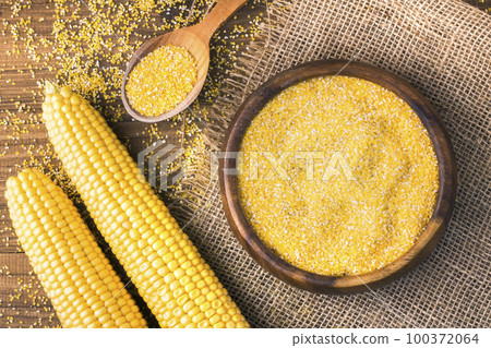 Corn grits in a wooden bowl on the background of fresh corn on the cob on a burlap. Corn grits in a wooden bowl on the background of fresh corn on the cob on a burlap. 100372064