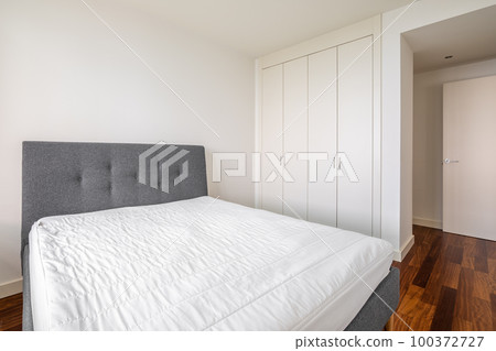 Double bed with wooden laminate floor and white walls and with built-in wardrobe on a sunny summer day. Concept of motel room or a bedroom after renovation. Copyspace Double bed with wooden laminate floor and white walls and with built-in wardrobe on a sunny summer day. Concept of motel room or a bedroom after renovation. Copyspace 100372727