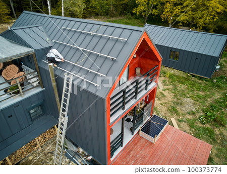 Man worker prepearing for mounting photovoltaic solar modules on roof of house. Roofer in helmet installing solar panel system outdoors. Concept of alternative and renewable energy. Man worker prepearing for mounting photovoltaic solar modules on roof of house. Roofer in helmet installing solar panel system outdoors. Concept of alternative and renewable energy. 100373774