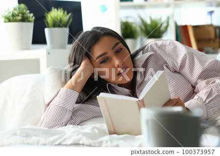 Beautiful woman lies in bed and reads book Beautiful woman lies in bed and reads book 100373957