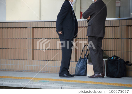 Two office workers waiting for a train at a station platform in winter 100375057