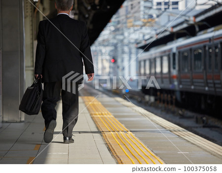 Rear view of a middle-aged office worker walking on the platform of the station in winter Rear view of a middle-aged office worker walking on the platform of the station in winter 100375058