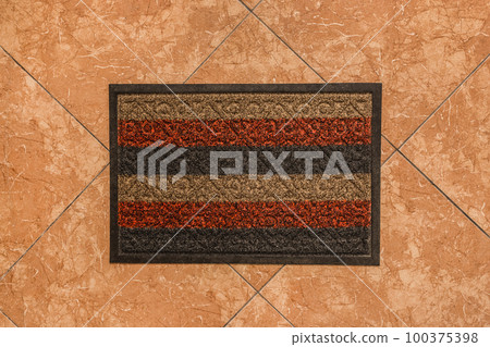 The rug for the feet of guests in the hallway on the background of a brown tiled floor texture, top view 100375398