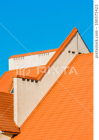 Geometric modern building facade exterior with orange tiled roof. Hotel against a blue sky Geometric modern building facade exterior with orange tiled roof. Hotel against a blue sky 100375423