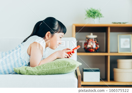 Elementary school girl looking at smartphone in living room Elementary school girl looking at smartphone in living room 100375522