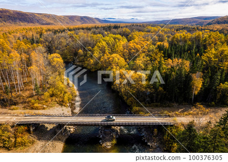 SUV on wooden bridge over small mountain river. Autumn forest. 100376305